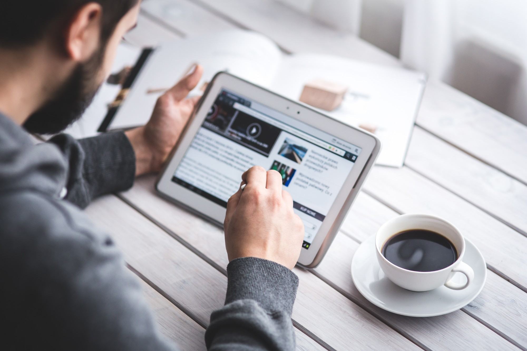 A reader going through market news on a tablet, with a cup of coffee on the table
