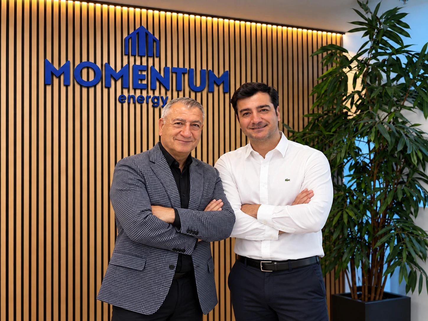 Two members of the Momentum Energy team in the office, in front of the company logo